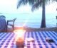 Romantic candlelit dinner setup on a white sand African beach at sunset with palm trees and ocean waves.