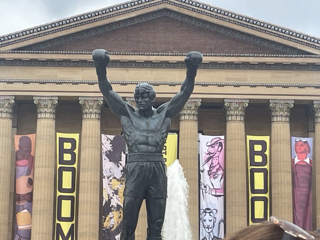 Bronze Rocky Balboa statue with outstretched arms at the base of the Philadelphia Museum of Art steps.