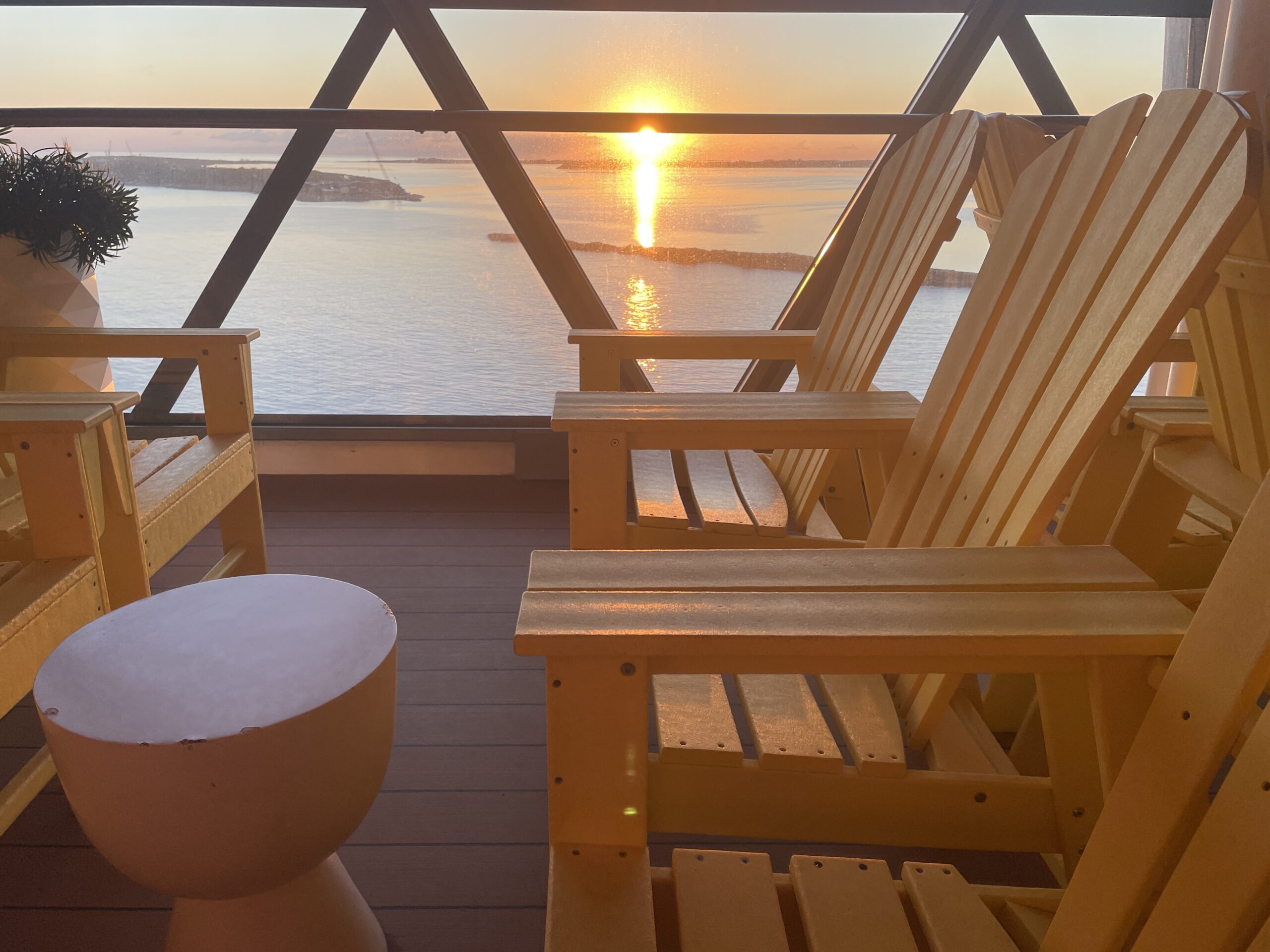 A peaceful orange and gold sunrise over the calm ocean as seen from the wooden loungers of a luxury cruise ship deck.