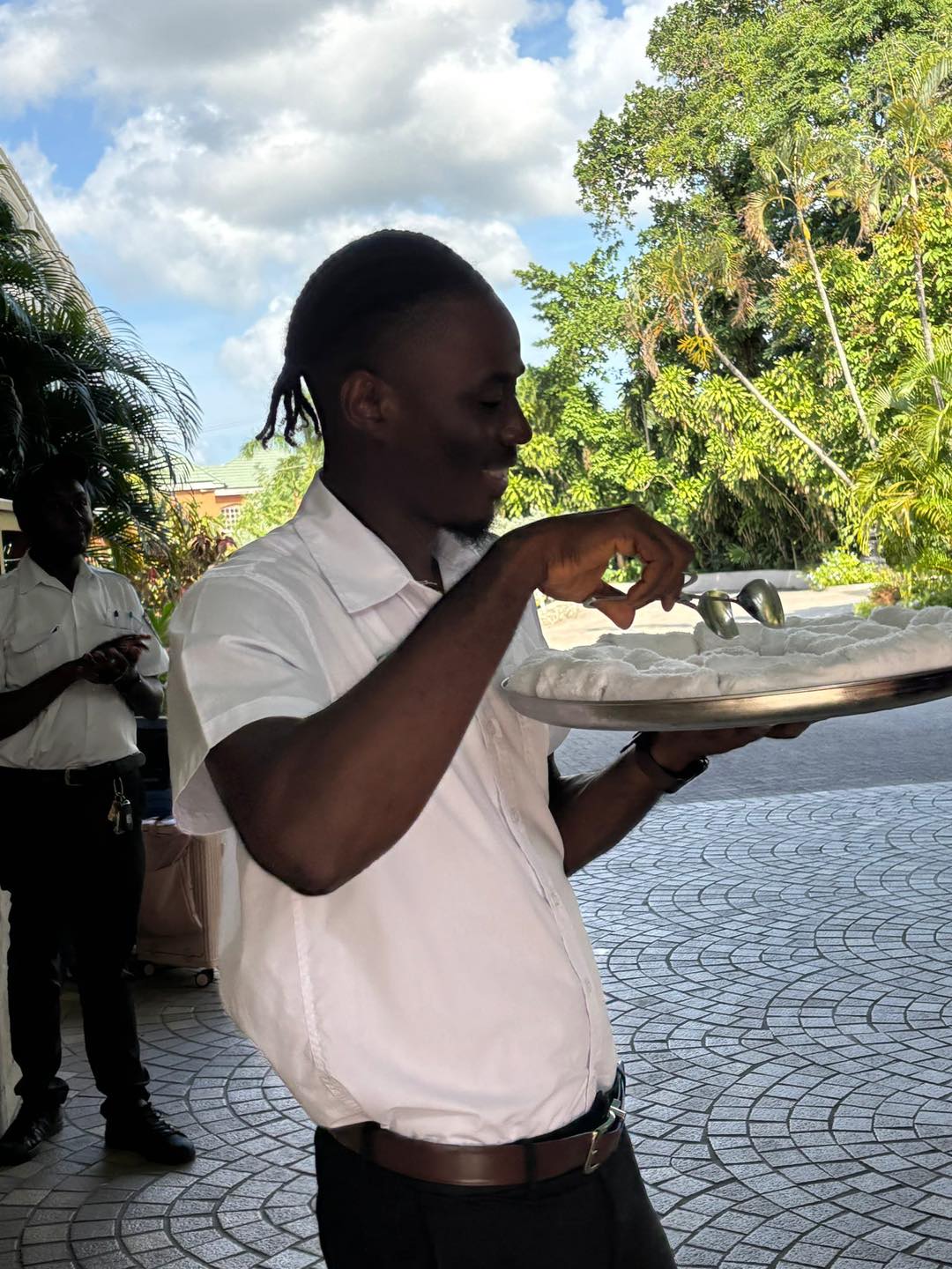 A professionally dressed Sandals Resorts butler serving lemongrass-scented hot towels to guests at a luxury all-inclusive resort.