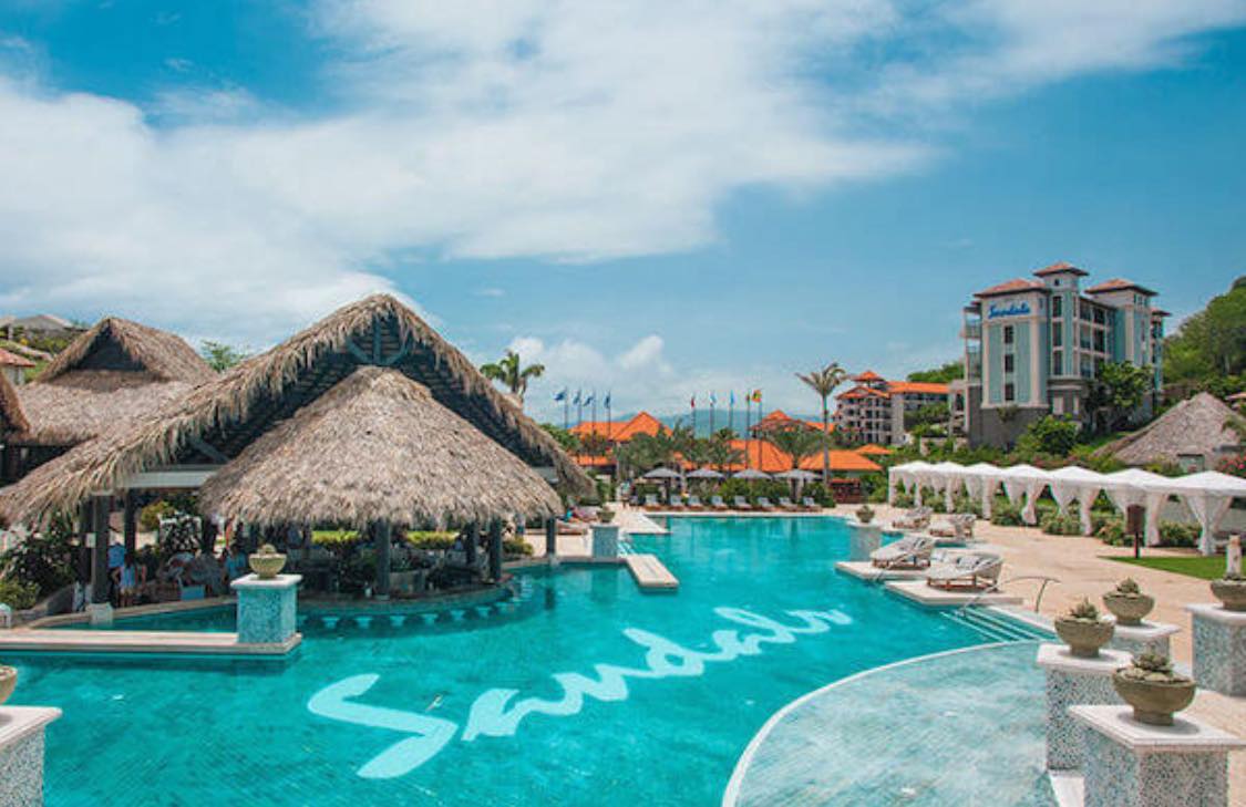 Sandals Resorts swim-up bar with premium spirits and thatched roof architecture in a crystal-clear lagoon pool.